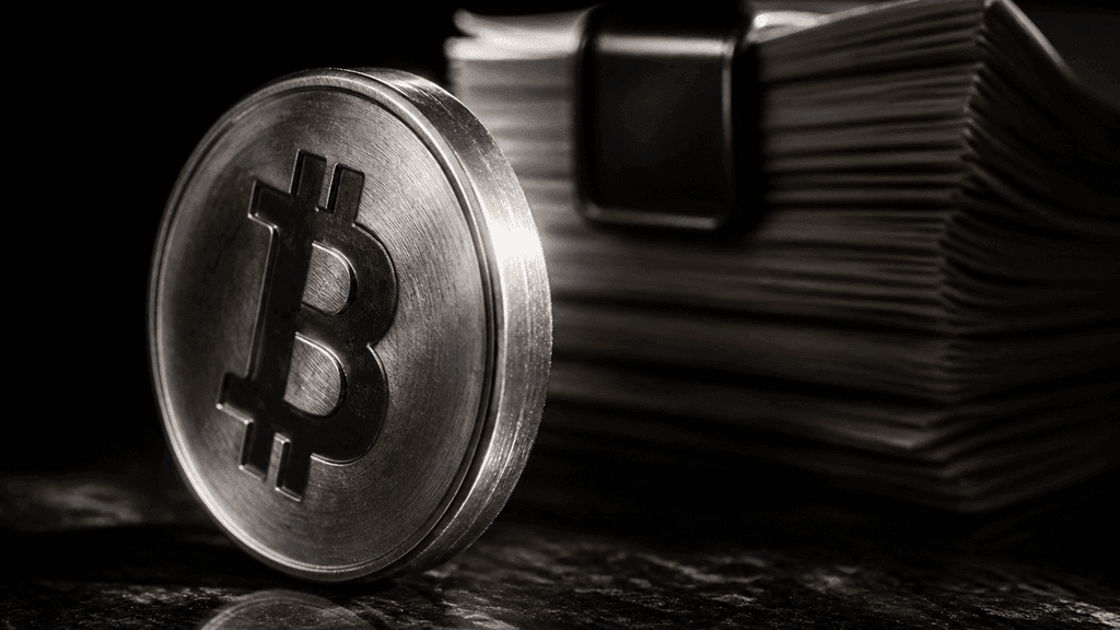Metallmünze mit eingeprägtem Bitcoin-Zeichen steht hochkant vor einem Stapel gebundener Antragsdokumente