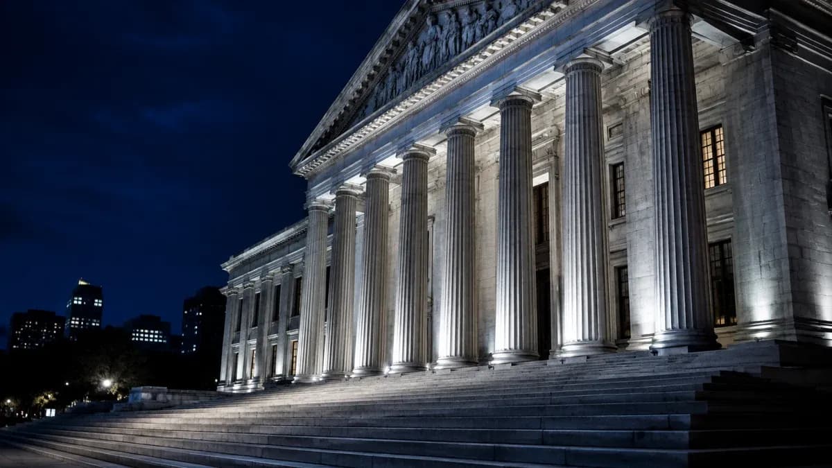 Behördengebäude mit hohen Steinsäulen bei Nacht, angestrahlt, leere Treppe davor