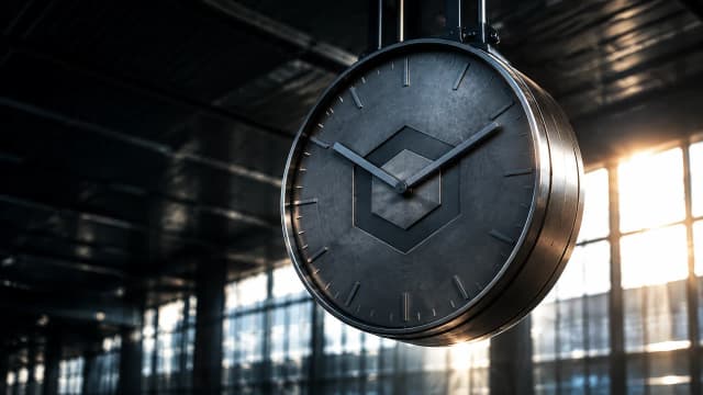 Grosse Bahnhofsuhr ohne Ziffern in einer leeren Halle, in das Metallgehaeuse ist das Chainlink-Zeichen eingraviert