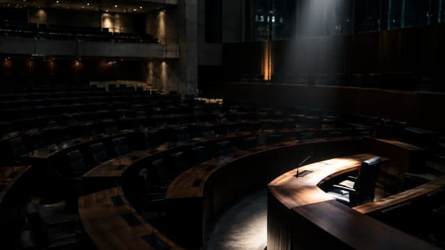 Leerer Plenarsaal einer europäischen Institution bei Nacht, ein einzelner Sitzplatz hell angestrahlt