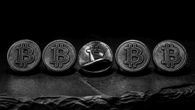 Fünf schwere Metallmarken mit eingeprägtem Bitcoin-Zeichen auf dunklem Stein, eine davon aus hohlem Blech und eingebrochen