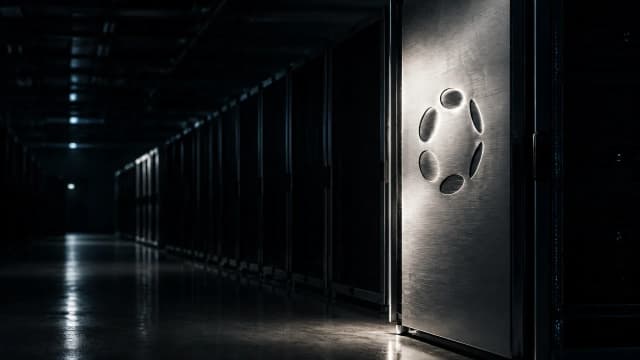 Weitgehend leergeräumter Serverraum bei Nacht, nur ein einzelner Schrank läuft noch, in seine Stahlfront ist das Polkadot-Zeichen eingraviert