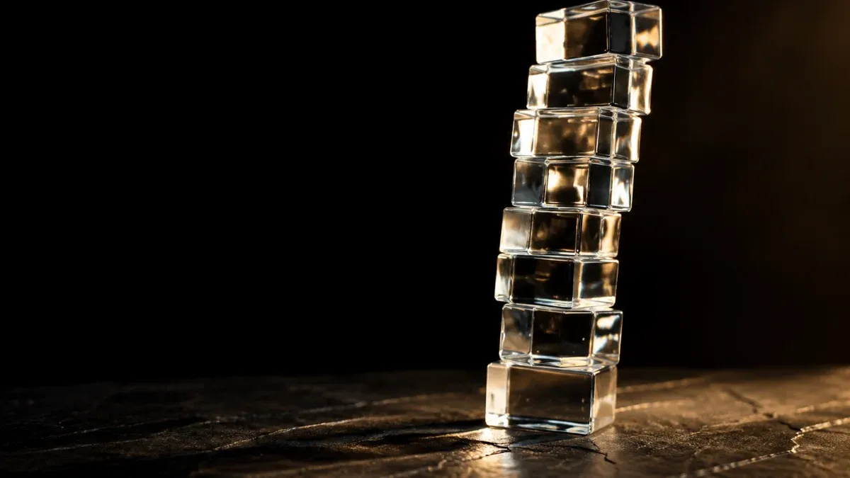 Hoher Turm aus Glasblöcken, der sich auf einem dunklen Tisch leicht zur Seite neigt
