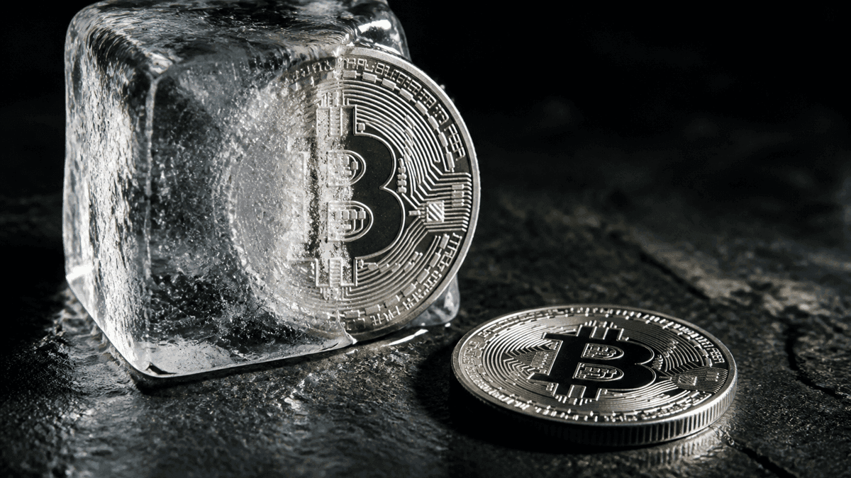 Silver coin half encased in a block of ice, next to a coin stamped with a Bitcoin symbol