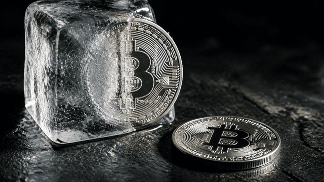 Silbermünze zur Hälfte in einem Eisblock eingeschlossen, daneben eine Münze mit eingeprägtem Bitcoin-Zeichen