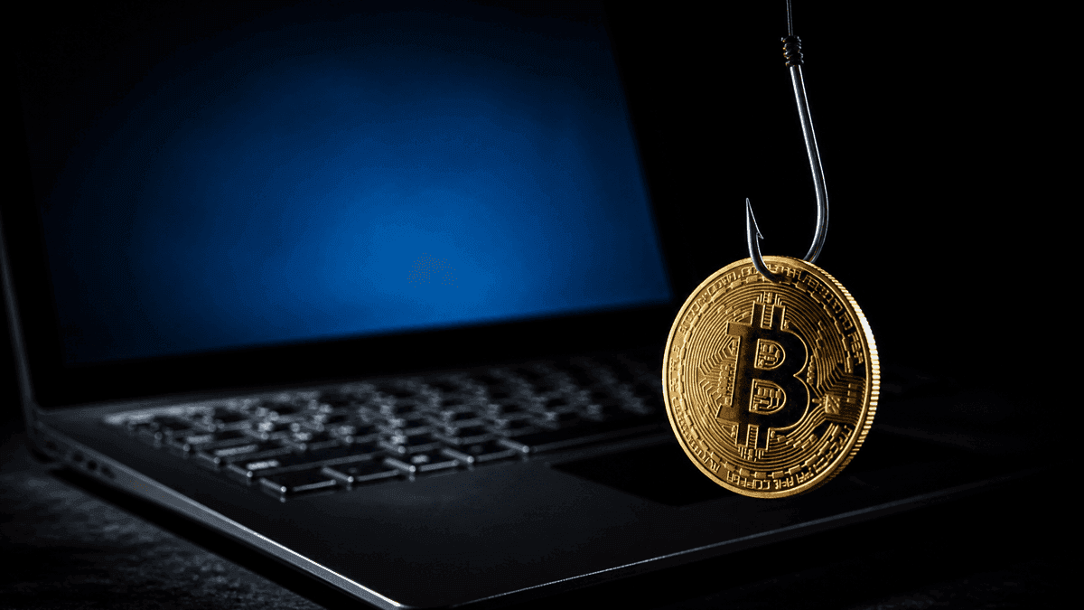 Eine goldene Münze mit Bitcoin-Symbol hängt an einem blanken Angelhaken über der Tastatur eines aufgeklappten Laptops im Dunkeln.