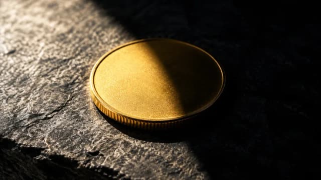 Goldmünze halb im Licht, halb im Schatten auf dunkler Steinplatte