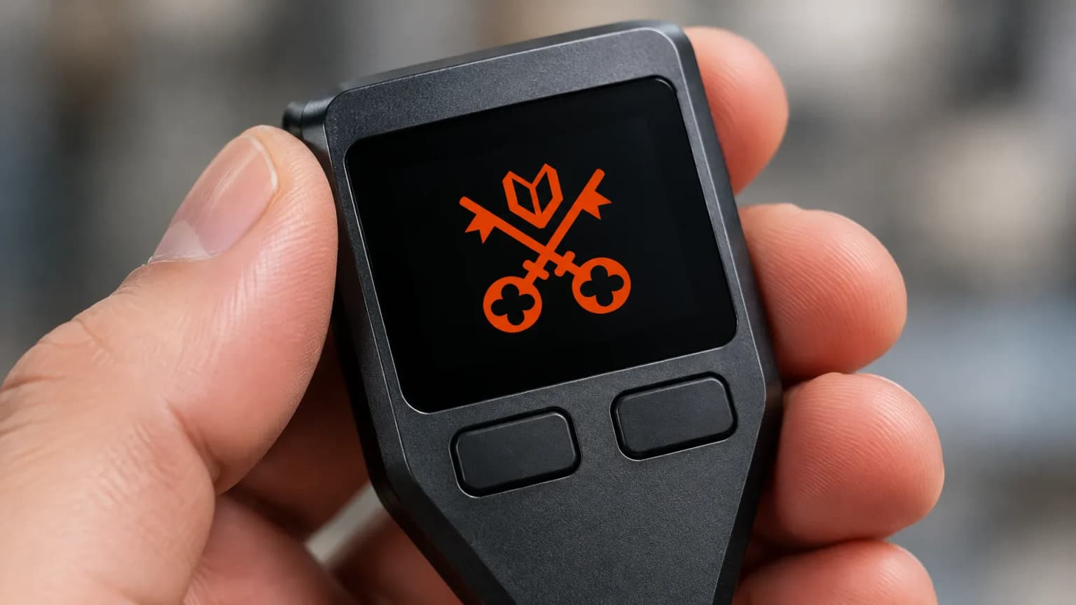 Branded-free hardware wallet held in one hand, the Venice Token sign with its crossed keys glowing orange on the dark display