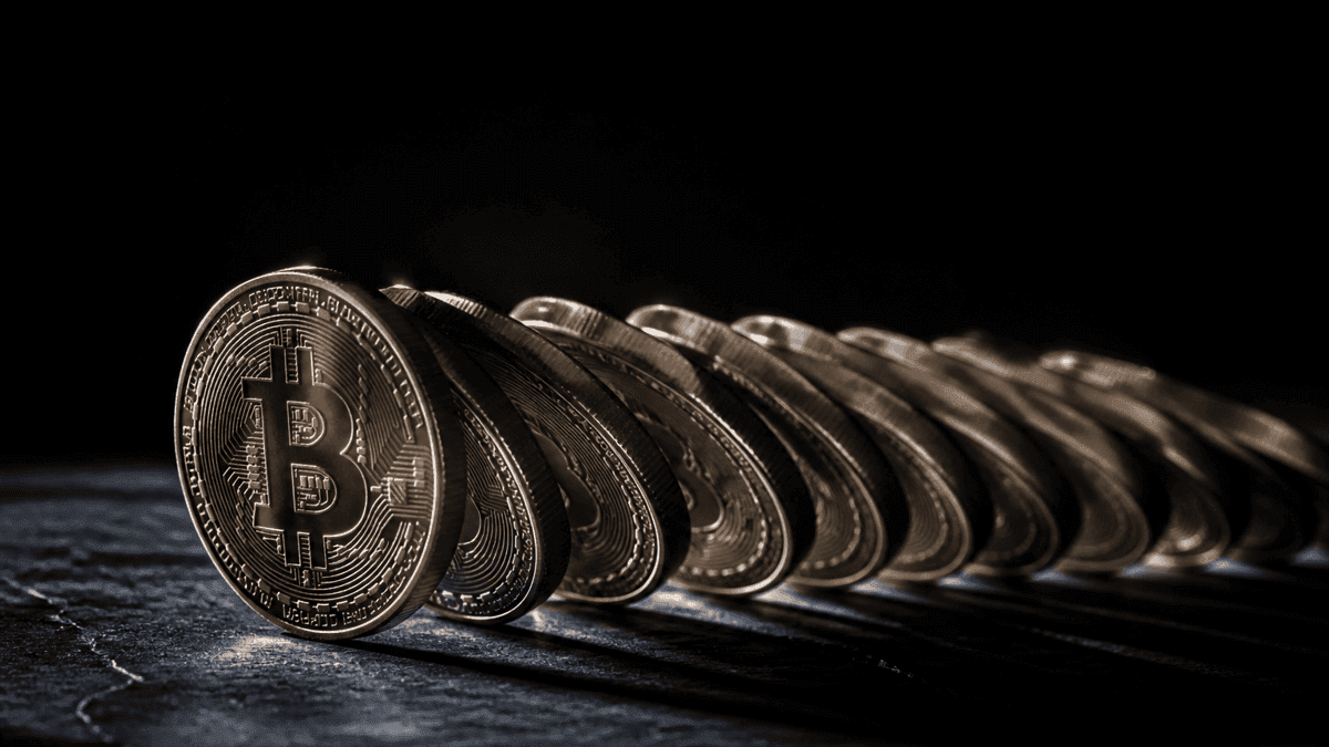 Eine Reihe physischer Münzen kippt geschlossen in dieselbe Richtung wie eine Dominoreihe, die vorderste Münze trägt das Bitcoin-Zeichen