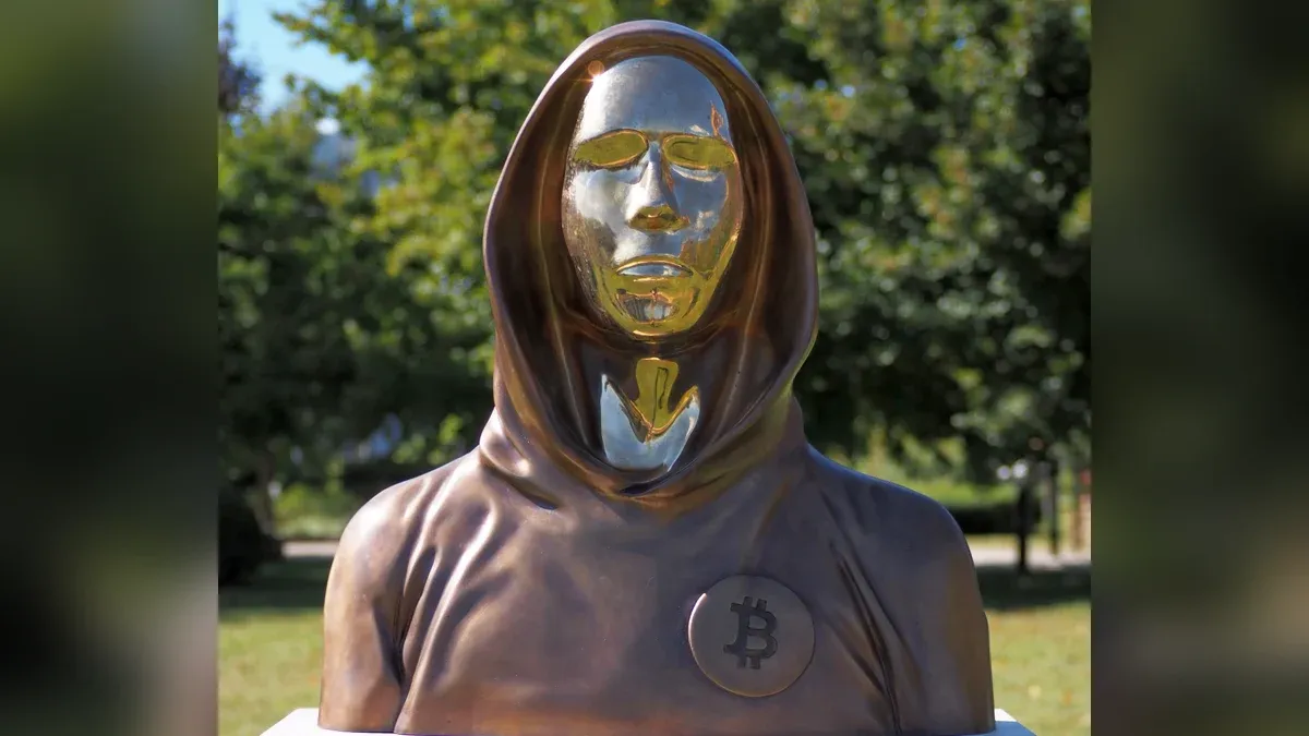 Bronzebüste von Satoshi Nakamoto mit Kapuze, spiegelndem Gesicht und Bitcoin-Zeichen auf der Brust im Graphisoft Park in Budapest