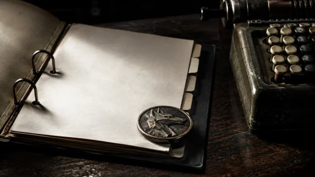 Aufgeschlagener Aktenordner mit leeren Registerlaschen, daneben ein mechanischer Tischrechner und eine Metallmuenze mit Tierkopf-Relief auf dunklem Holz