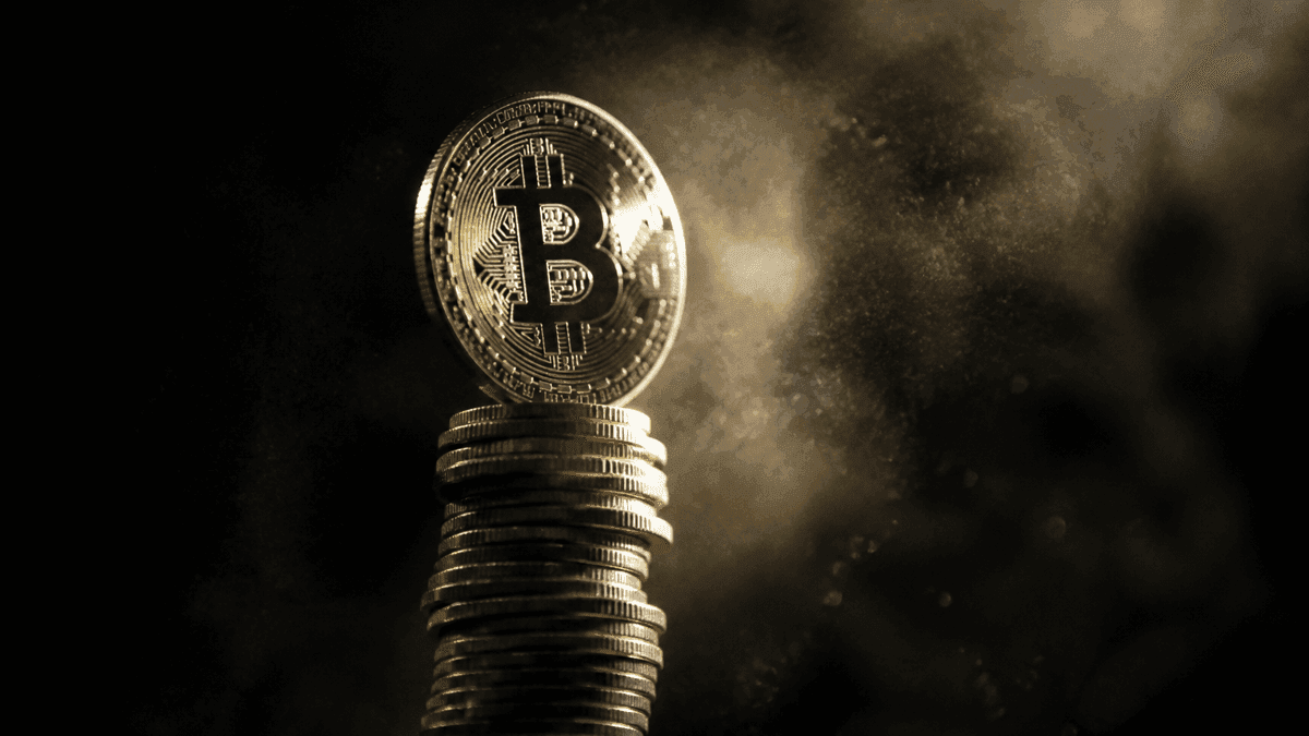 Hochglanzpolierte Metallmünze mit eingeprägtem Bitcoin-Zeichen balanciert auf der Spitze eines steil aufragenden Münzturms